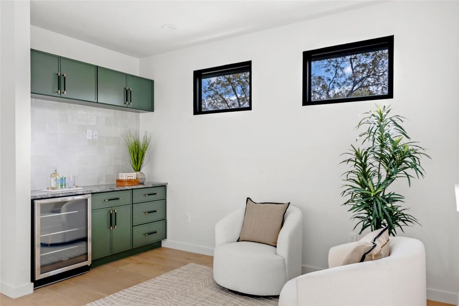 Bar featuring green cabinetry, beverage cooler, light wood-type flooring, tasteful backsplash, and light stone counters