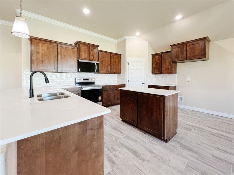 Kitchen with decorative backsplash, appliances with stainless steel finishes, a kitchen island, pendant lighting, and light stone countertops Kitchen with decorative backsplash, appliances with stainless steel finishes, a kitchen island, pendant lighting, and light stone countertops