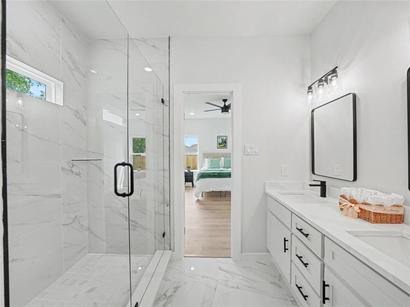 Ensuite bathroom featuring light marble finish flooring, double vanity, a marble finish shower, and healthy amount of natural light