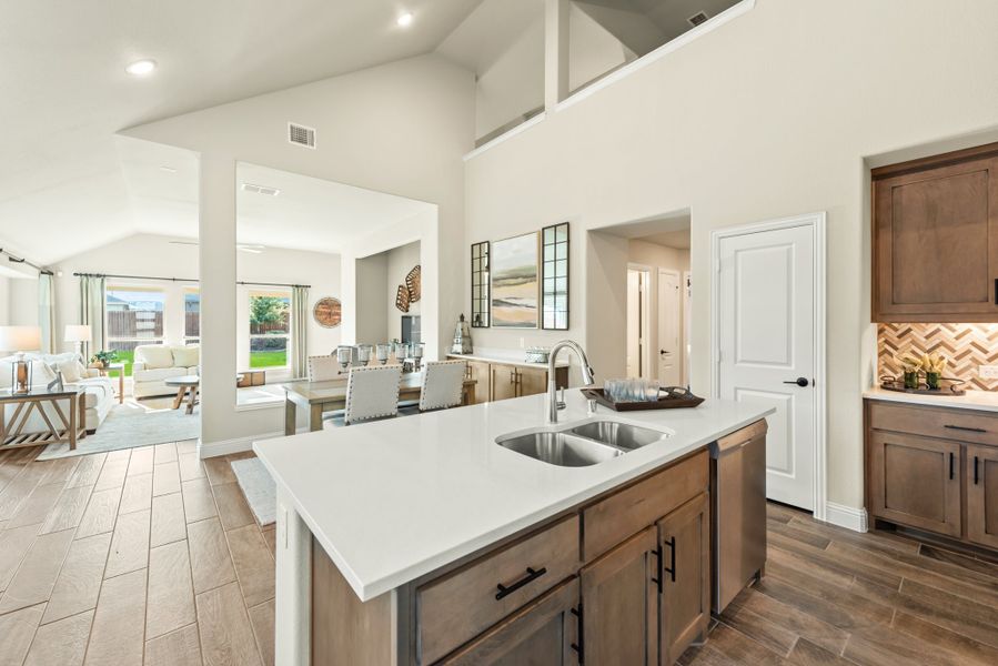 Kitchen island with double sink and white countertop, open floor plan with dining and living areas visible beyond