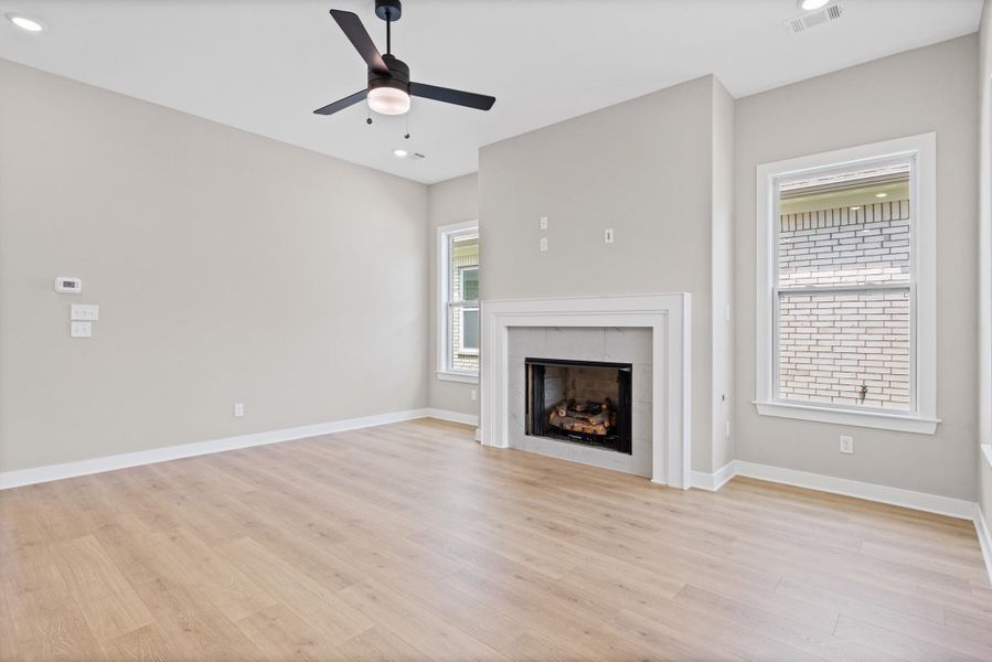 Spacious living area featuring a fireplace with a white mantel, wood-finish flooring, recessed lighting, and a ceiling fan Spacious living area featuring a fireplace with a white mantel, wood-finish flooring, recessed lighting, and a ceiling fan