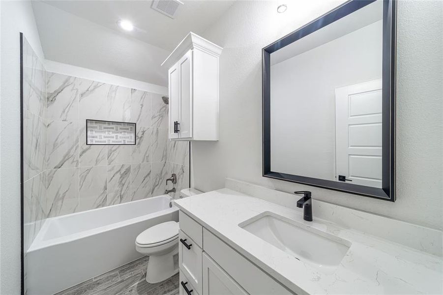 Bathroom featuring toilet, wood finished floors, vanity, visible vents, and washtub / shower combination