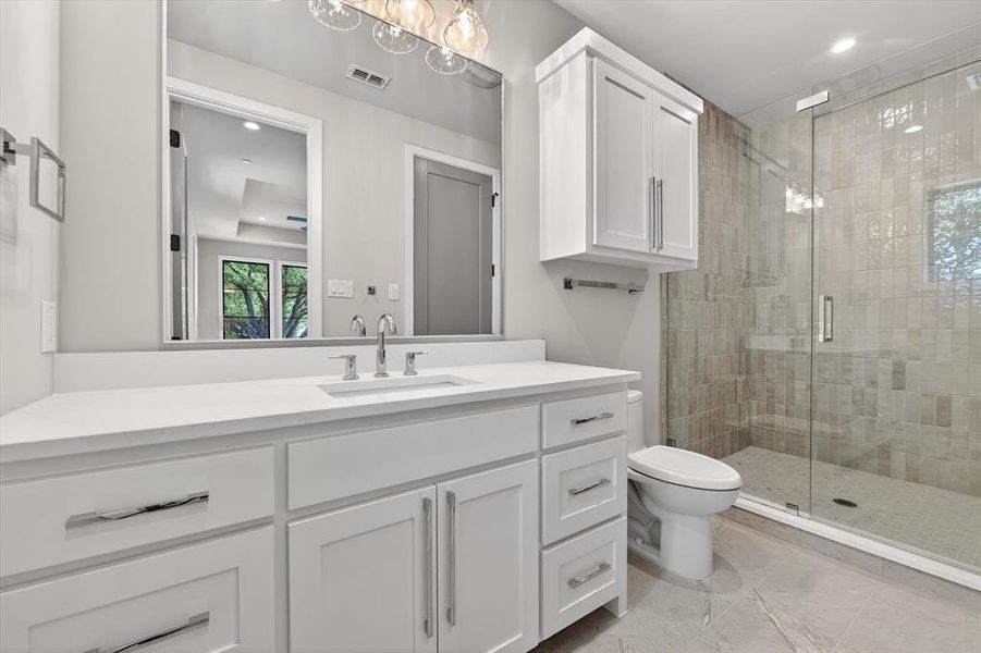 Bathroom featuring a white vanity with a recessed sink, a walk-in shower with a glass enclosure, white cabinetry, and gray tile flooring Bathroom featuring a white vanity with a recessed sink, a walk-in shower with a glass enclosure, white cabinetry, and gray tile flooring