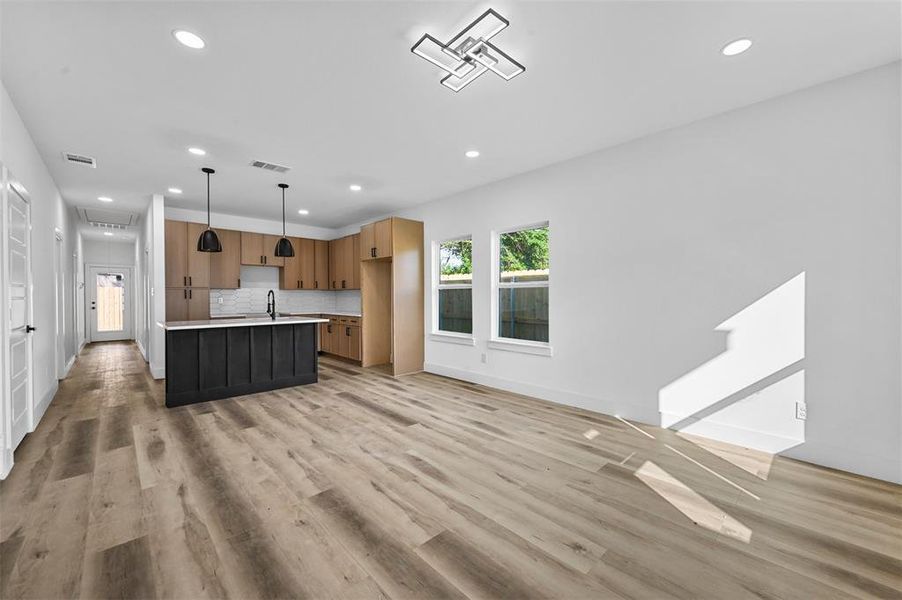 Kitchen with light hardwood / wood-style floors, hanging light fixtures, tasteful backsplash, an island with sink, and sink