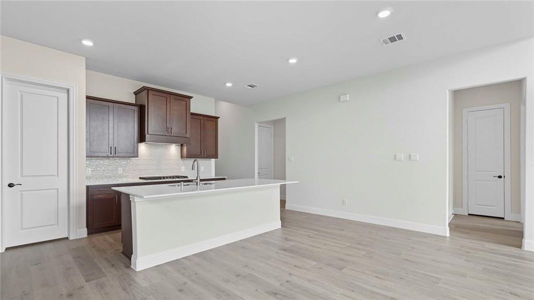 Open-concept kitchen featuring an island with a breakfast bar, dark wood cabinetry, a tile backsplash, and light wood-finish flooring