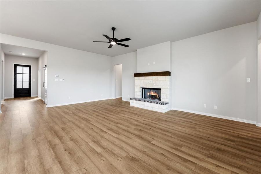 Unfurnished living room with light wood-type flooring, a stone fireplace, and a ceiling fan Unfurnished living room with light wood-type flooring, a stone fireplace, and a ceiling fan