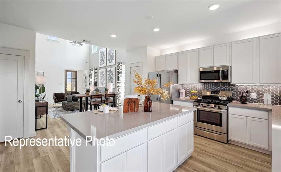The kitchen features a spacious island with a light-toned countertop, white cabinetry, stainless steel appliances, and a honeycomb-patterned backsplash