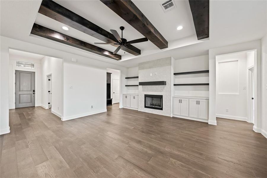 Unfurnished living room featuring ceiling fan, a fireplace, light wood finished floors, beamed ceiling, and recessed lighting
