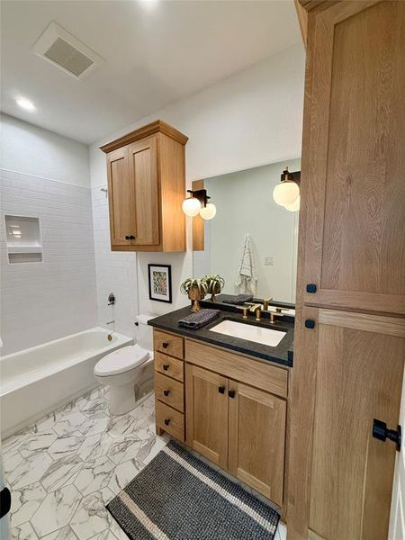 Bathroom featuring a light wood-finish vanity with a dark countertop, an undermount sink, and brass-finish fixtures