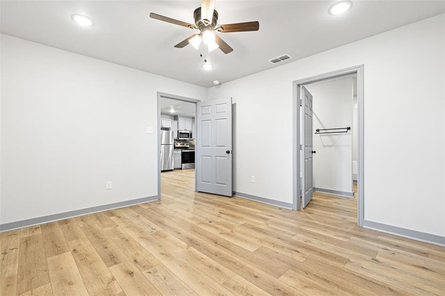 Unfurnished bedroom featuring light wood-type flooring, ceiling fan, recessed lighting, freestanding refrigerator, and a walk in closet Unfurnished bedroom featuring light wood-type flooring, ceiling fan, recessed lighting, freestanding refrigerator, and a walk in closet