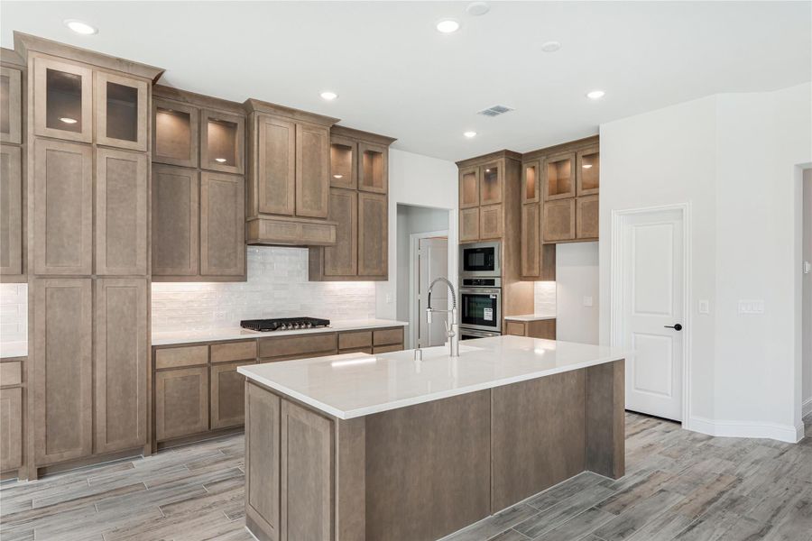 Kitchen with tall brown wood cabinets, center island with white countertop, and stainless steel double ovens