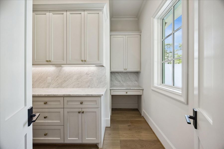 Expansive walk-in pantry featuring marble slab backsplash, custom cabinetry with soft-close drawers and doors, and under-cabinet lighting. Built-in workstation adds functionality, creating a refined and highly organized prep space.