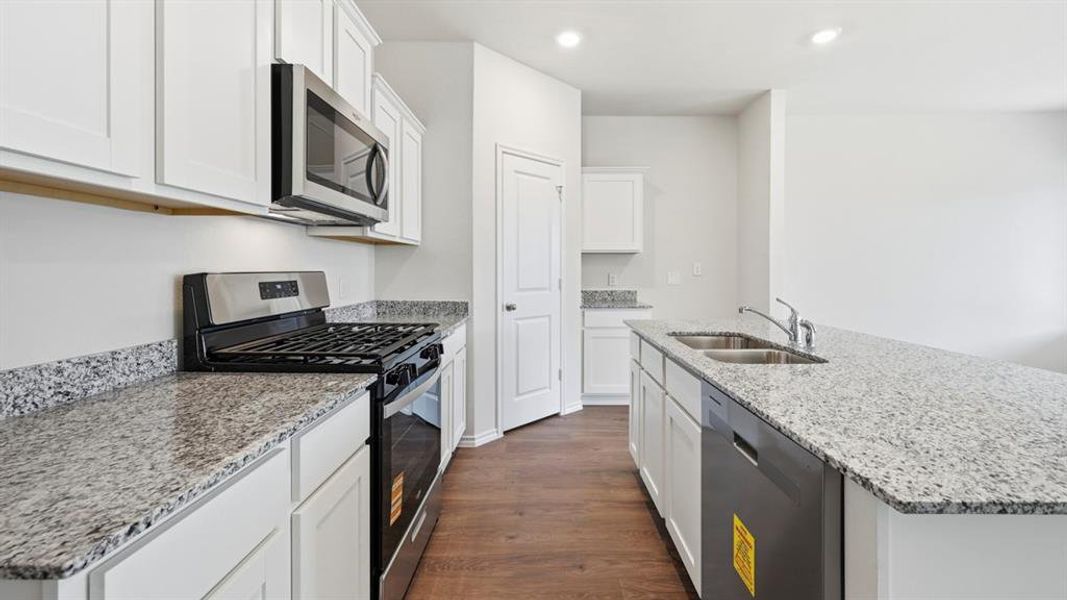 Kitchen featuring stainless steel appliances, white cabinetry, light stone countertops, a kitchen island with sink, and dark wood-style flooring