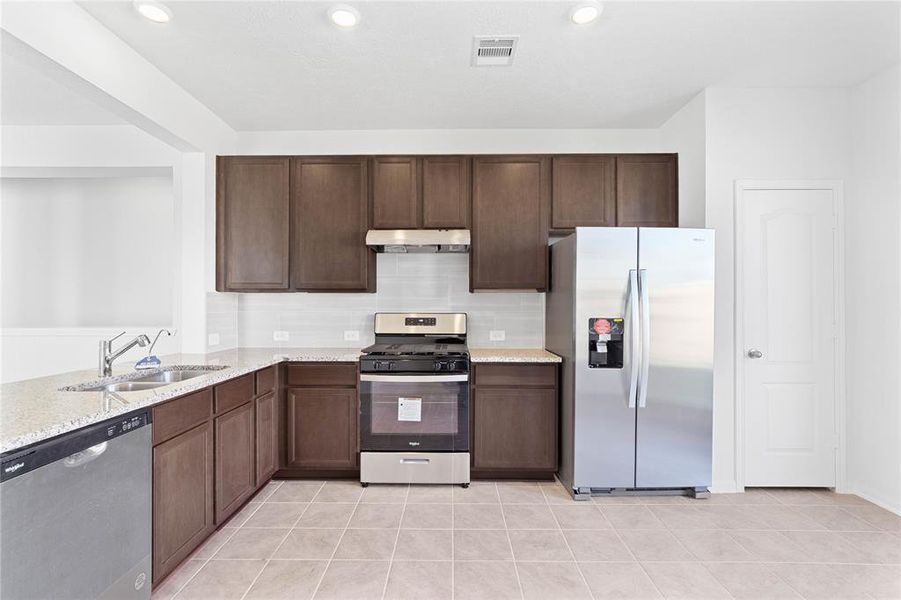 This spacious kitchen features high ceilings, stained wood cabinets, granite countertops, SS appliances, modern tile backsplash, recessed lighting, and a walk-in pantry all overlooking your huge family room.