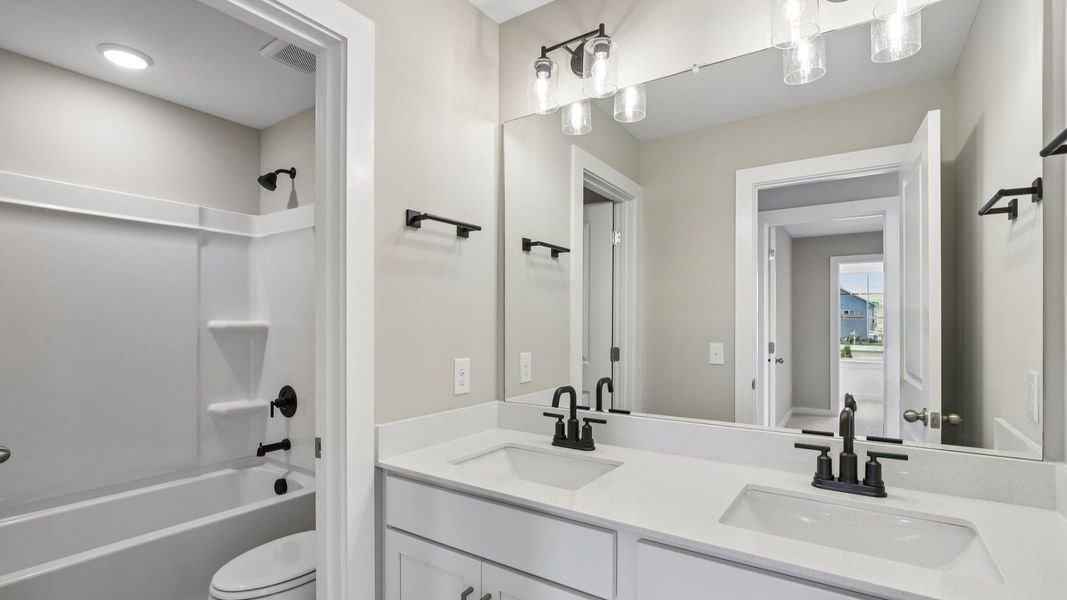 Secondary Bathroom with dual vanity and door to shower and toilet
