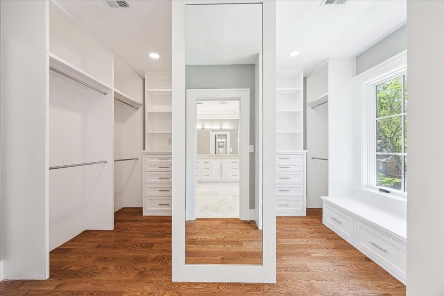 This is just part of the spacious walk-in primary bedroom walk-in closet and features hardwood floors, ample shelving, hanging space, and a large mirror. It includes built-in drawers and a window seat with storage, offering plenty of natural light.