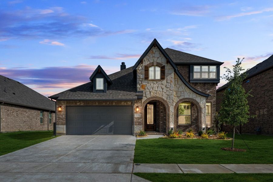 Two-story home with stone and brick exterior, two-car garage, arched entry, and manicured lawn at dusk