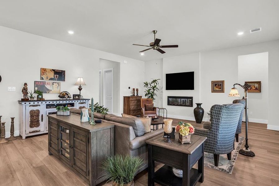 Open-concept living space featuring ceiling fan, ample natural light from multiple windows, an inset electric fireplace, and wood-finish flooring