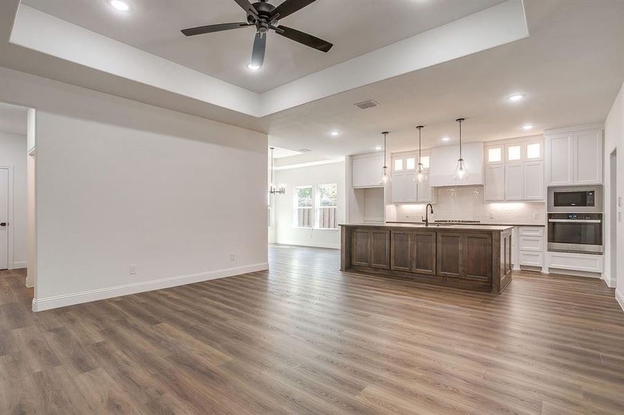 Unfurnished living room with dark wood finished floors, a ceiling fan, recessed lighting, a chandelier, and a tray ceiling