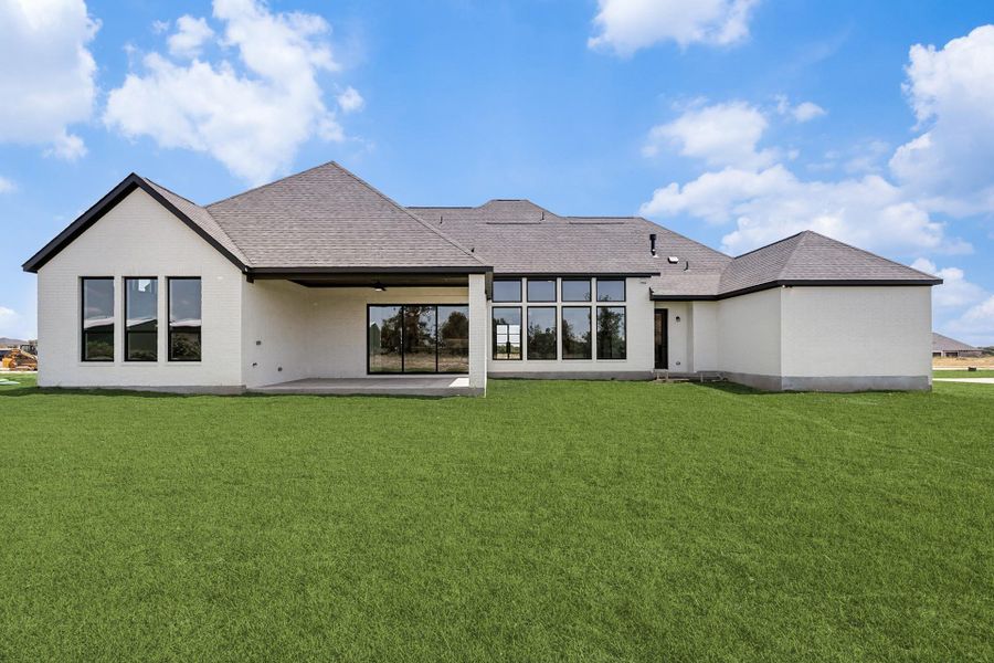 An expansive green lawn stretches behind a modern brick home with a covered back patio.