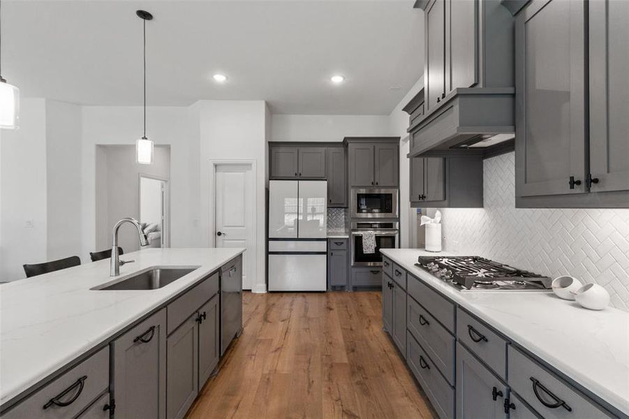Kitchen with pendant lighting, tasteful backsplash, stainless steel appliances, light wood-style floors, and gray cabinetry