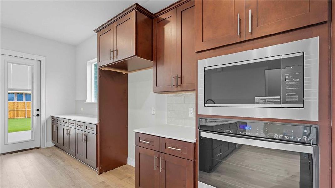 Kitchen featuring dark wood cabinetry, light countertops, wood-finish flooring, a built-in stainless steel microwave, and a built-in stainless steel oven