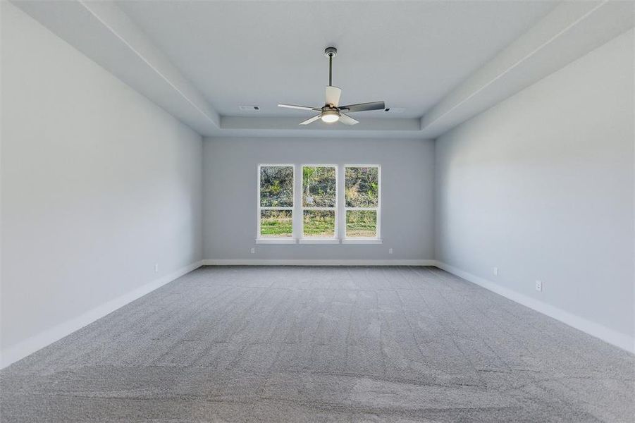 Unfurnished room with ceiling fan, light colored carpet, and a tray ceiling