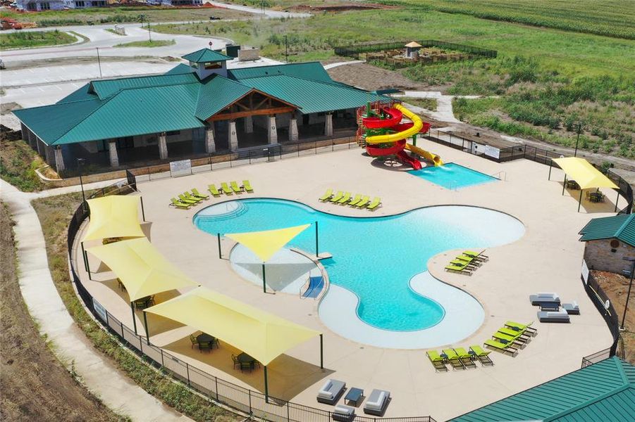 Expansive community pool area featuring a large freeform swimming pool, separate children's pool with colorful waterslides, and a clubhouse with a green metal roof