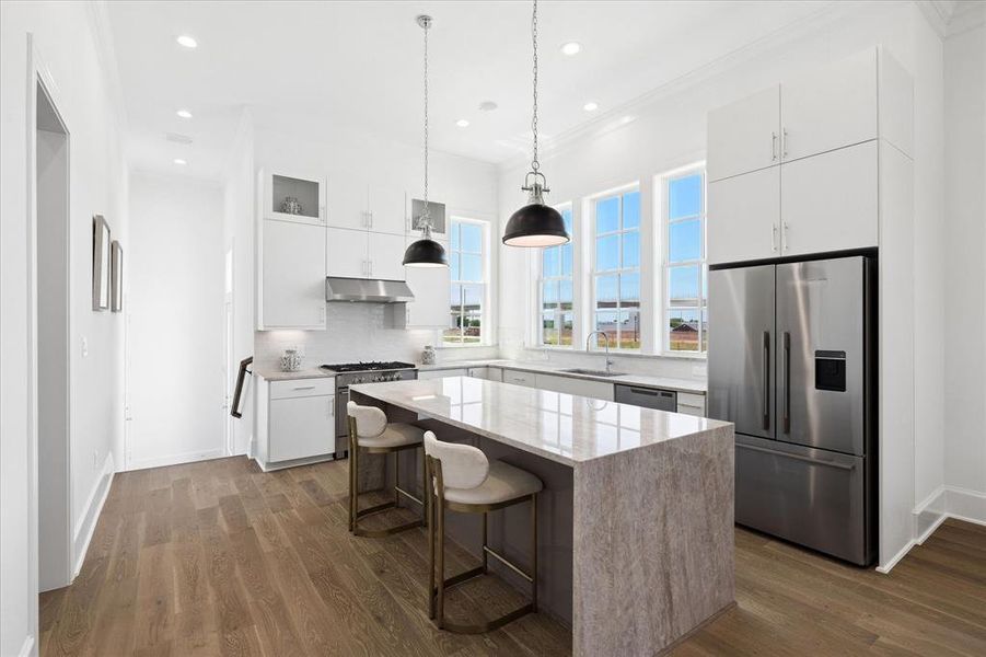Contemporary kitchen featuring an oversized island with countertop seating, stainless steel appliances, white cabinetry, and three large windows