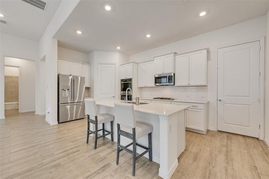Kitchen featuring stainless steel appliances, a center island with sink, backsplash, a kitchen bar, and white cabinetry Kitchen featuring stainless steel appliances, a center island with sink, backsplash, a kitchen bar, and white cabinetry