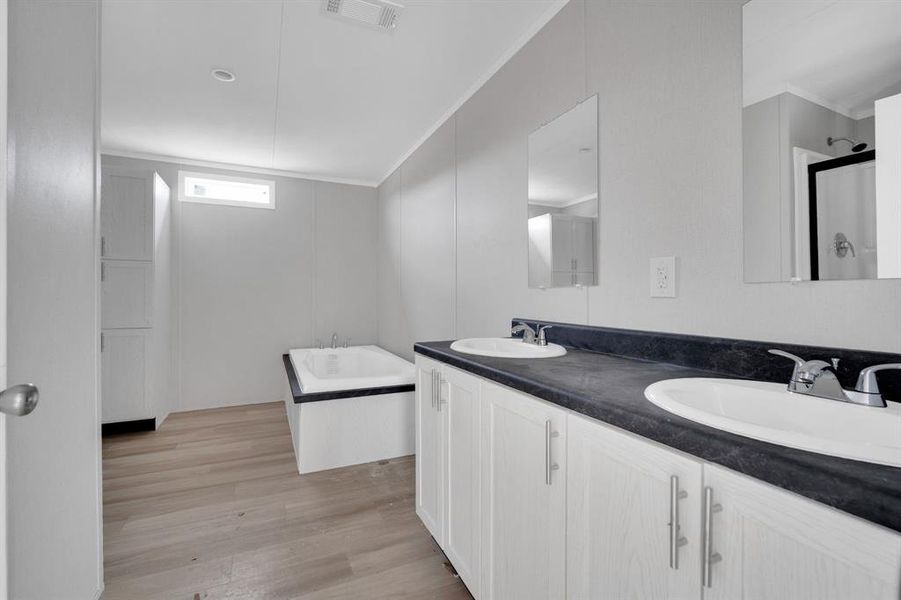 Bathroom with a garden tub, light wood-style floors, double vanity, crown molding, and a shower stall