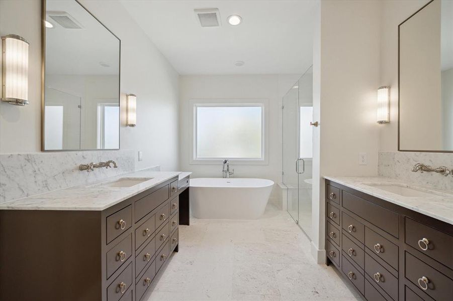 The primary ensuite exudes luxury and sophistication with its carefully curated design. Dual vanities with marble countertops and wall-mounted fixtures offer elegance and ample storage. A freestanding soaking tub creates a serene focal point, paired with a frosted window for privacy. Frameless glass encloses the shower, featuring a bench and rainfall showerhead for a spa-like experience. Polished nickel accents and custom cabinetry elevate the design, combining functionality with timeless sophistication.