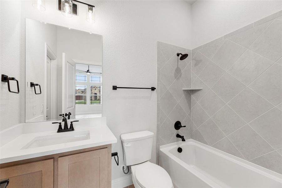 Bathroom with wood vanity, white countertop, and tub-shower combo with gray diagonal tile and black fixtures Bathroom with wood vanity, white countertop, and tub-shower combo with gray diagonal tile and black fixtures