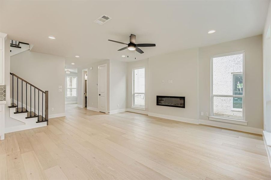 Unfurnished living room featuring stairway, light wood finished floors, recessed lighting, ceiling fan, and a glass covered fireplace