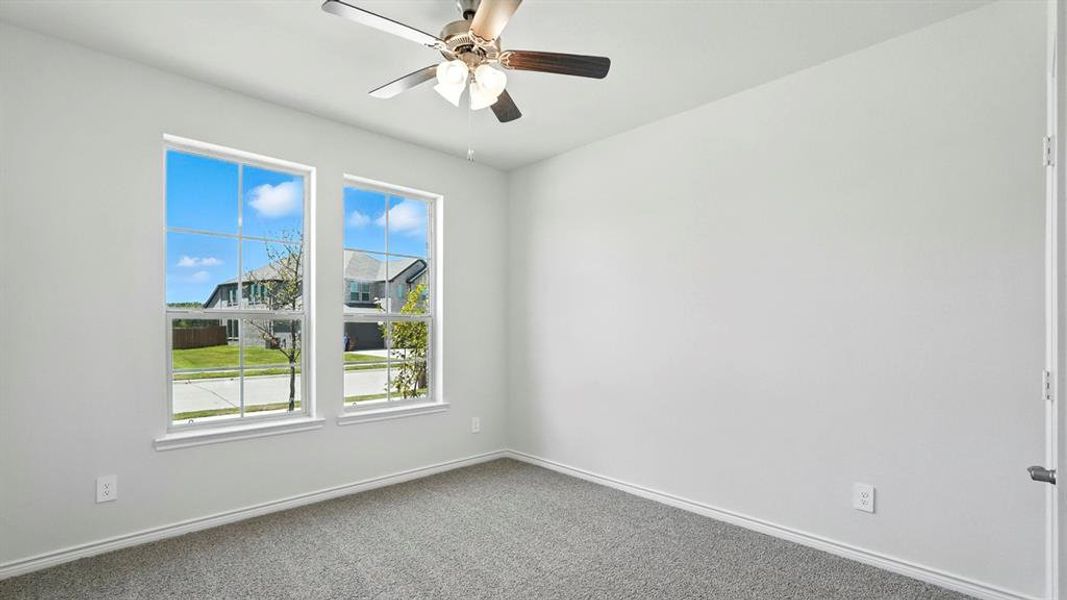 Bright interior room featuring two large windows, gray carpet, white baseboards, and a ceiling fan with integrated lighting Bright interior room featuring two large windows, gray carpet, white baseboards, and a ceiling fan with integrated lighting