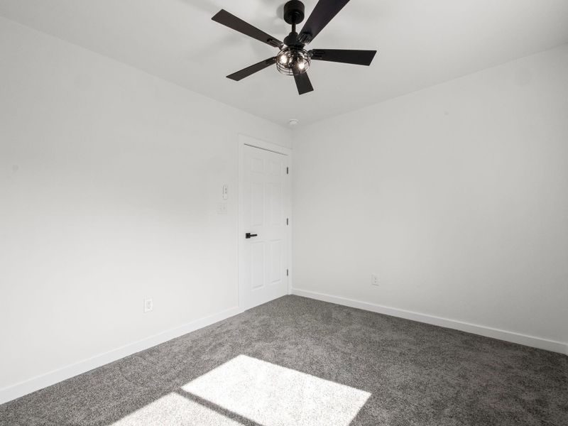 Room featuring light gray carpet flooring, white walls, and a modern black ceiling fan with integrated lighting