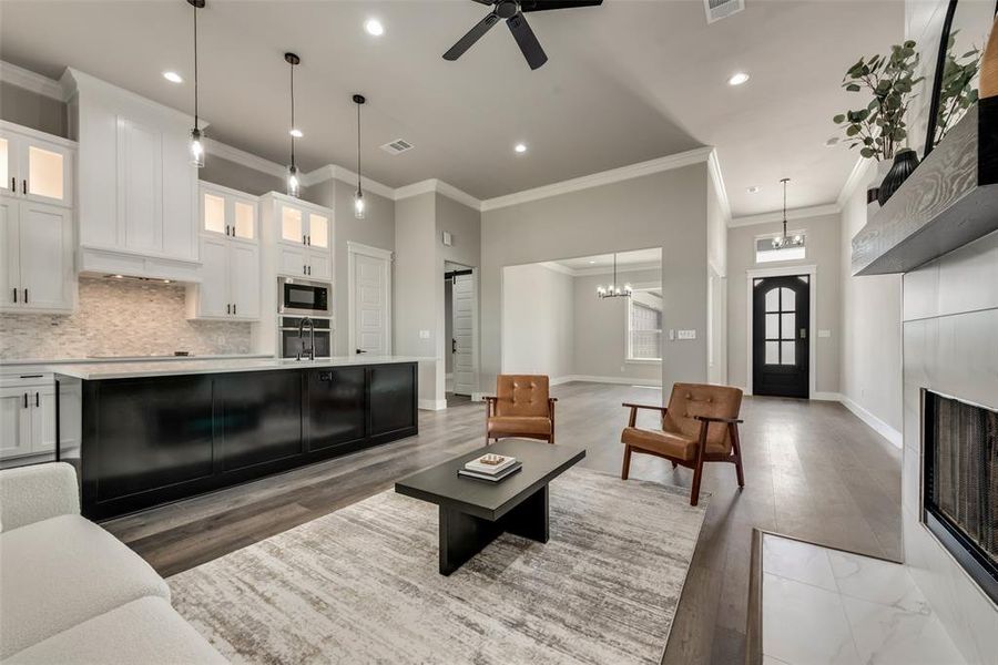 Living room with light wood-type flooring, crown molding, ceiling fan with notable chandelier, and sink