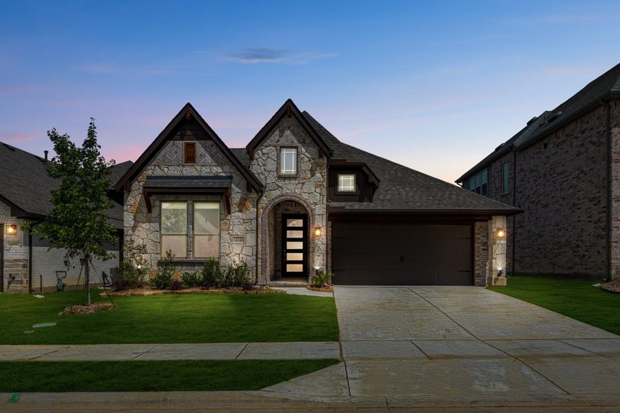 Single-story home with stone exterior, arched entry, two-car garage, and manicured lawn at dusk Single-story home with stone exterior, arched entry, two-car garage, and manicured lawn at dusk