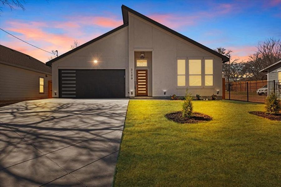 View of front of house featuring stucco siding, fence, a garage, driveway, and a front lawn