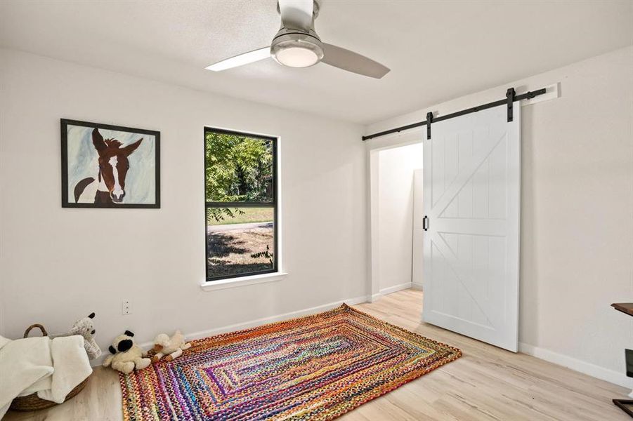 Bedroom featuring a barn door, ceiling fan, and light wood-type flooring