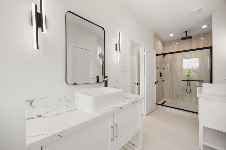 A polished view of the primary bath showcasing dual vanities with individual mirrors, dual showerheads, designer lighting, and stylish flooring.