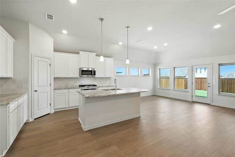 Kitchen with a center island with sink, white cabinets, decorative backsplash, dark wood finished floors, and pendant lighting Kitchen with a center island with sink, white cabinets, decorative backsplash, dark wood finished floors, and pendant lighting