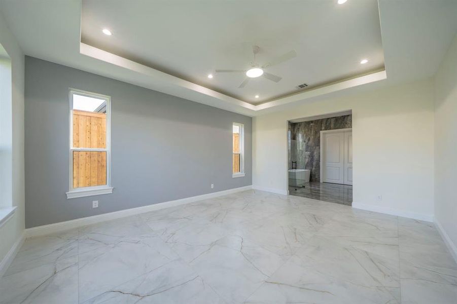 Unfurnished bedroom with light marble finish flooring, a raised ceiling, recessed lighting, and ceiling fan Unfurnished bedroom with light marble finish flooring, a raised ceiling, recessed lighting, and ceiling fan