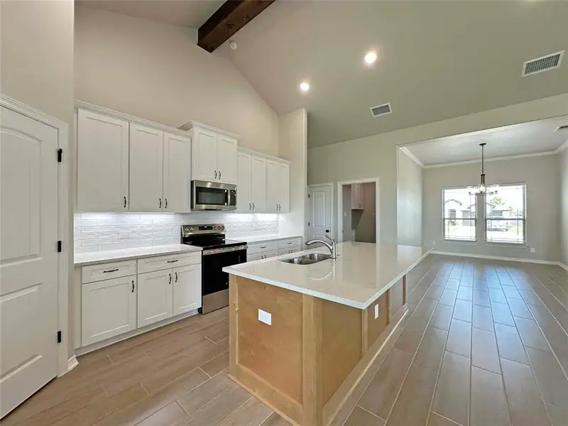 Kitchen featuring backsplash, appliances with stainless steel finishes, white cabinets, high vaulted ceiling, and wood finish floors Kitchen featuring backsplash, appliances with stainless steel finishes, white cabinets, high vaulted ceiling, and wood finish floors