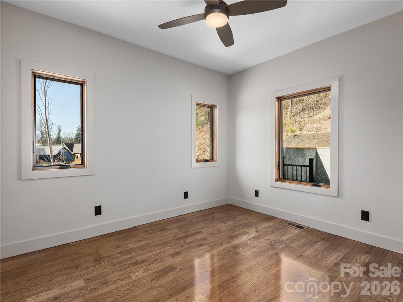 Bedroom two on the main level featuring oak hardwood floors, ceiling fan, and abundant natural light.