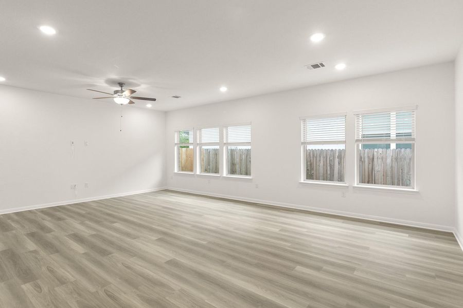 Spacious room featuring light-toned flooring, white walls, multiple windows, recessed lighting, and a ceiling fan