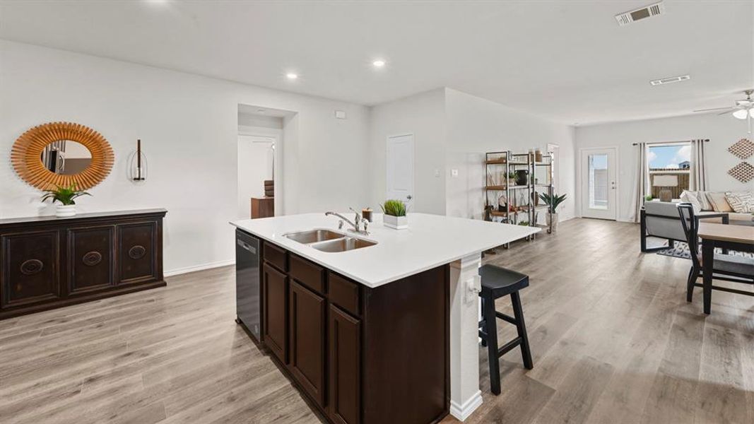 The open-concept living area features light-toned flooring, recessed lighting, and a kitchen island with a white countertop and a double sink