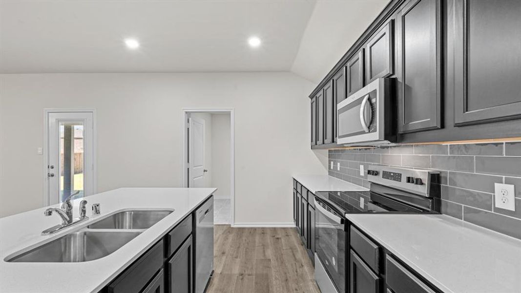Modern kitchen featuring dark cabinetry, stainless steel appliances, a grey subway tile backsplash, light countertops, and recessed lighting