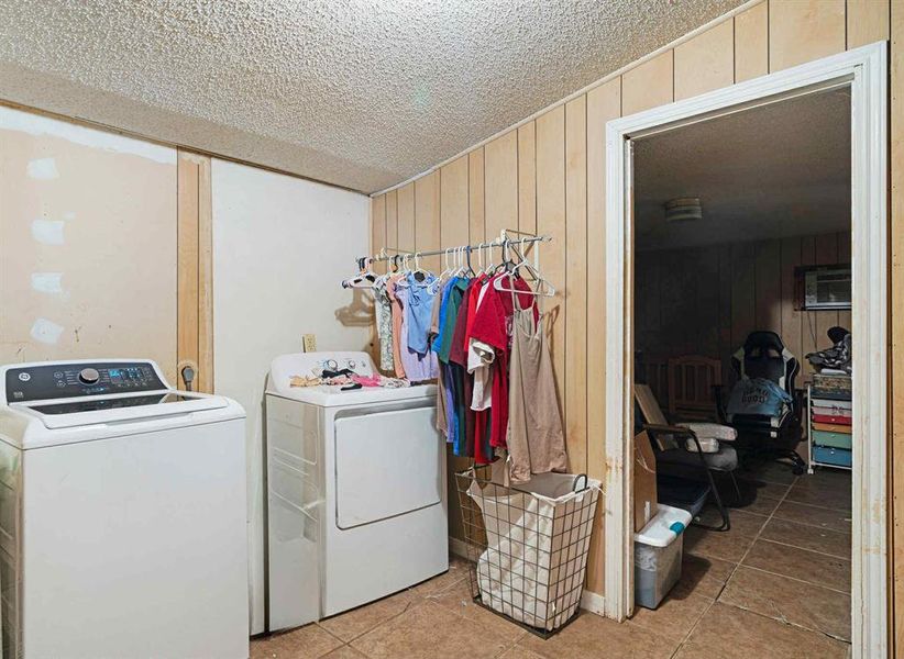 Laundry room featuring wood walls, light tile patterned floors, a textured ceiling, and washing machine and dryer Laundry room featuring wood walls, light tile patterned floors, a textured ceiling, and washing machine and dryer