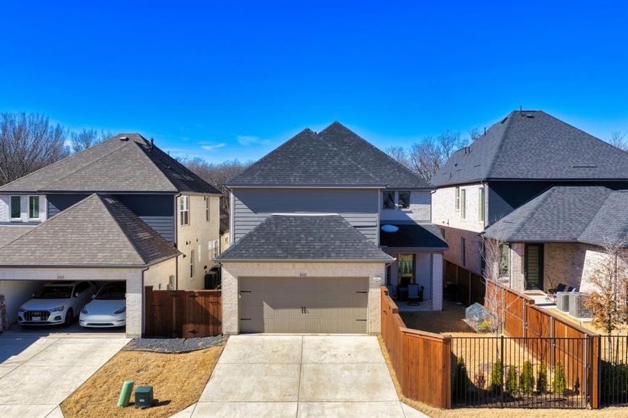 View of front of home with roof with shingles, driveway, a patio, and a gate